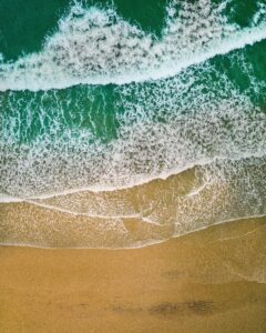 Breathtaking aerial view of vibrant ocean waves crashing onto the golden sandy beach.